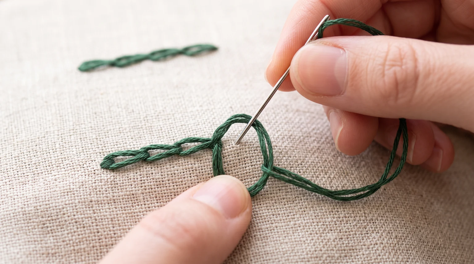 Needle and working loop beside a short line of green chain stitches