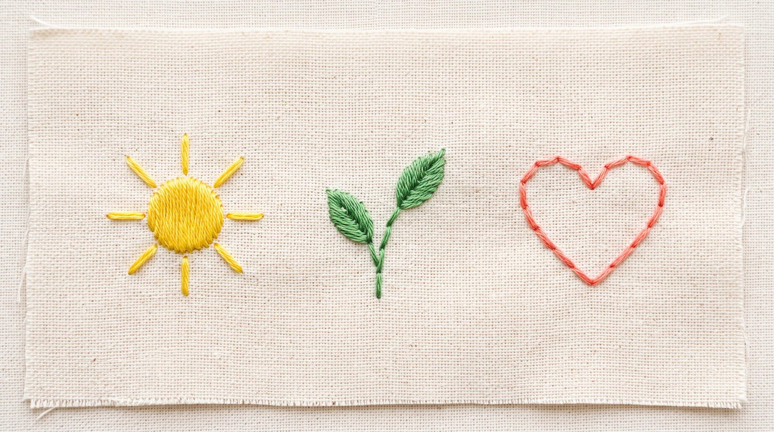 Three small embroidery examples: yellow sun, green sprig and coral heart outline