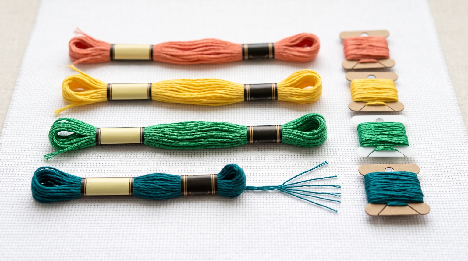 Coral, yellow, green and teal floss skeins beside matching bobbins and separated teal strands