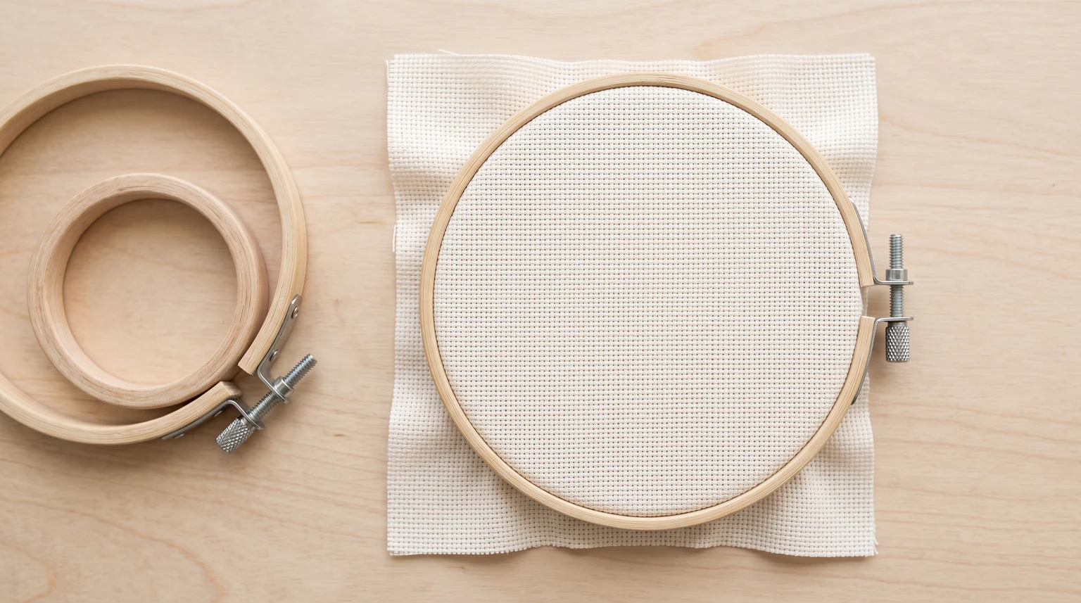 Wooden hoop holding evenly spread woven fabric beside two empty hoop rings