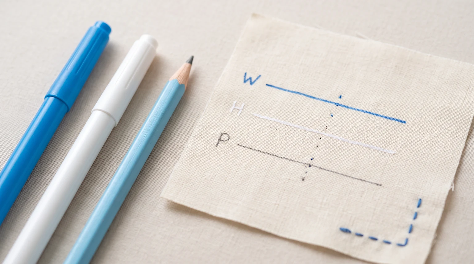 Two fabric marking pens and a pencil beside trial lines on a small cloth swatch