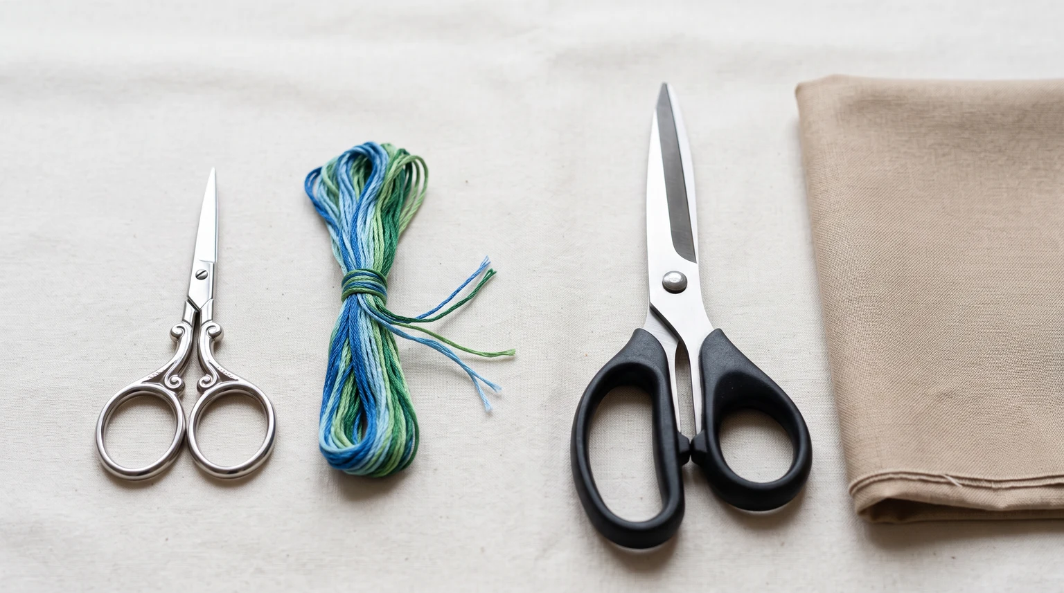 Small embroidery scissors beside larger fabric shears, floss and folded cloth