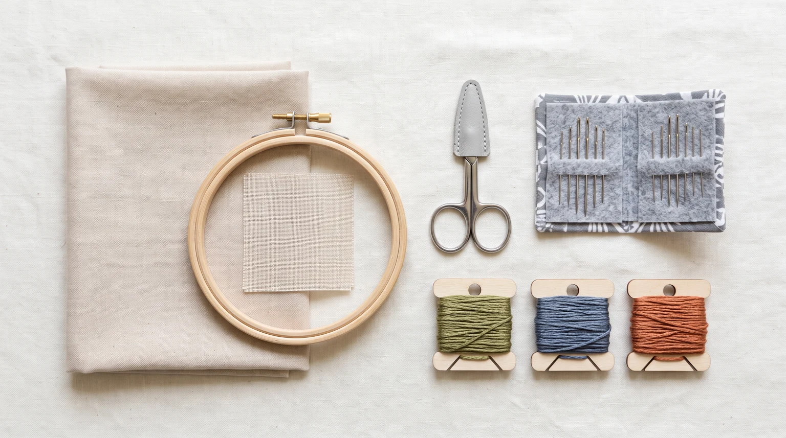 Folded fabric, hoop, scissors, needle packets and three organized floss bobbins