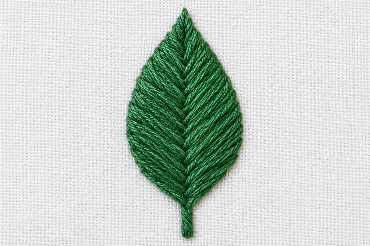 Finished emerald green fishbone leaf with diagonal stitches meeting along a narrow central vein