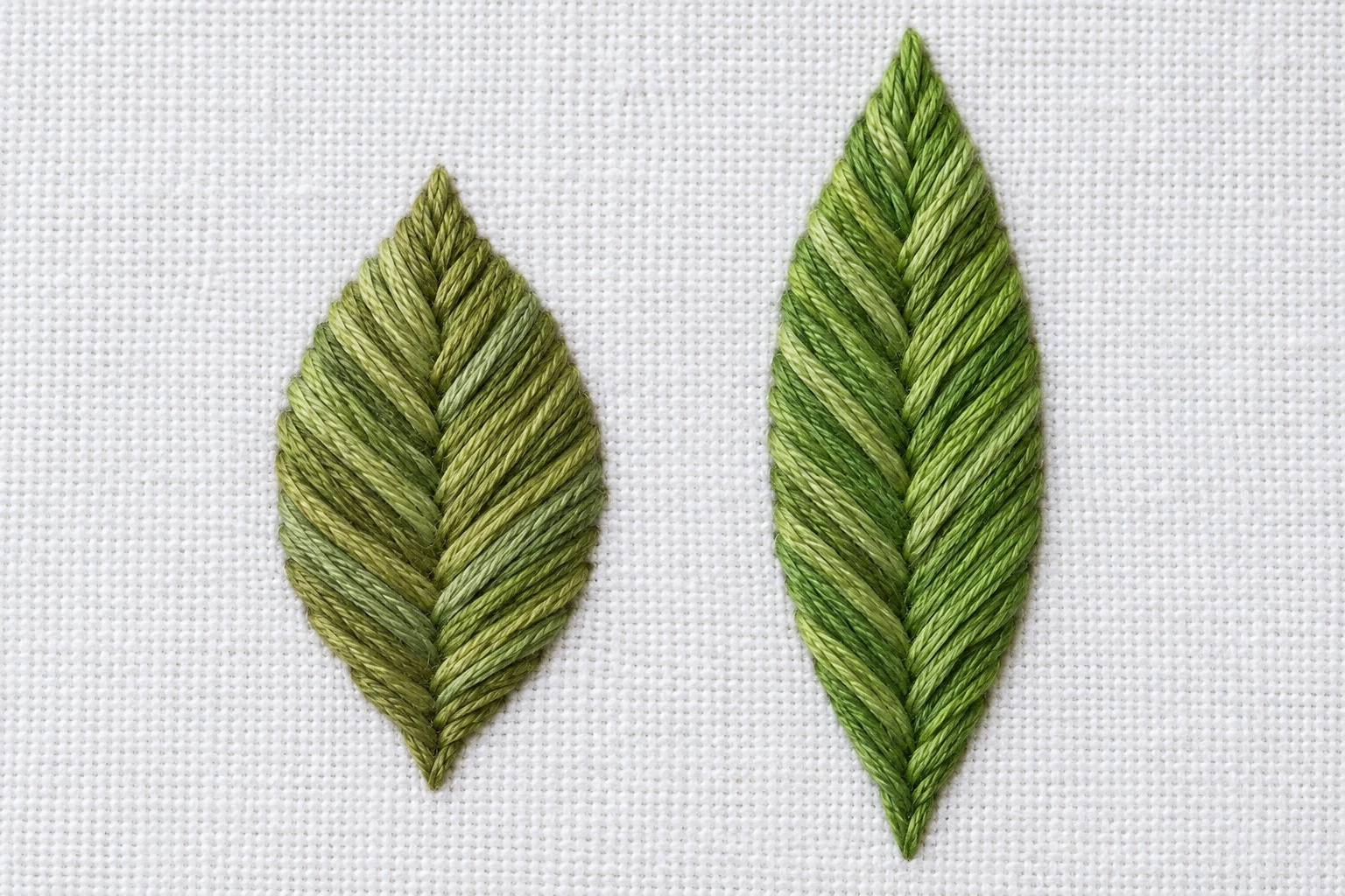 Two green fishbone leaves of different proportions with balanced central veins and orderly diagonal stitches