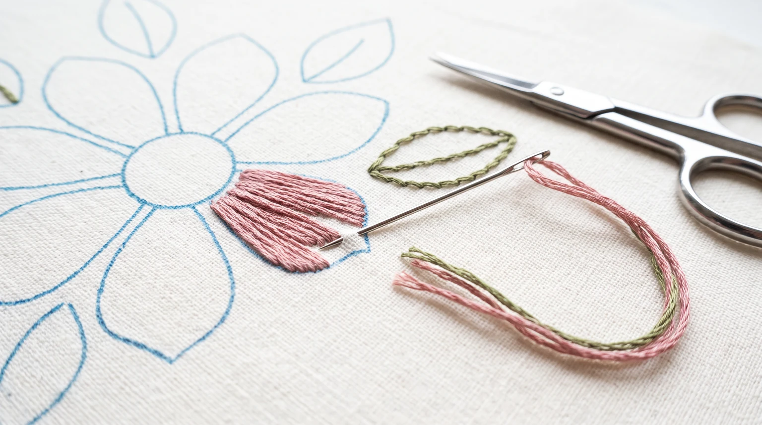 Close view of a floral outline on fabric with one pink filled petal and a separate green stitched leaf sample