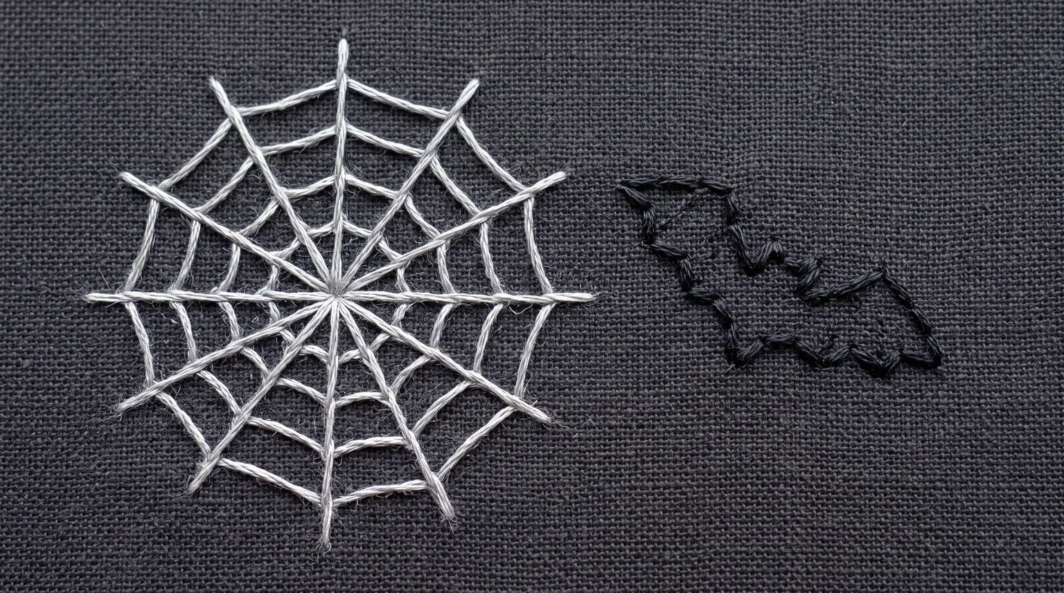 Pale stitched spiderweb beside a dark outlined bat on gray fabric