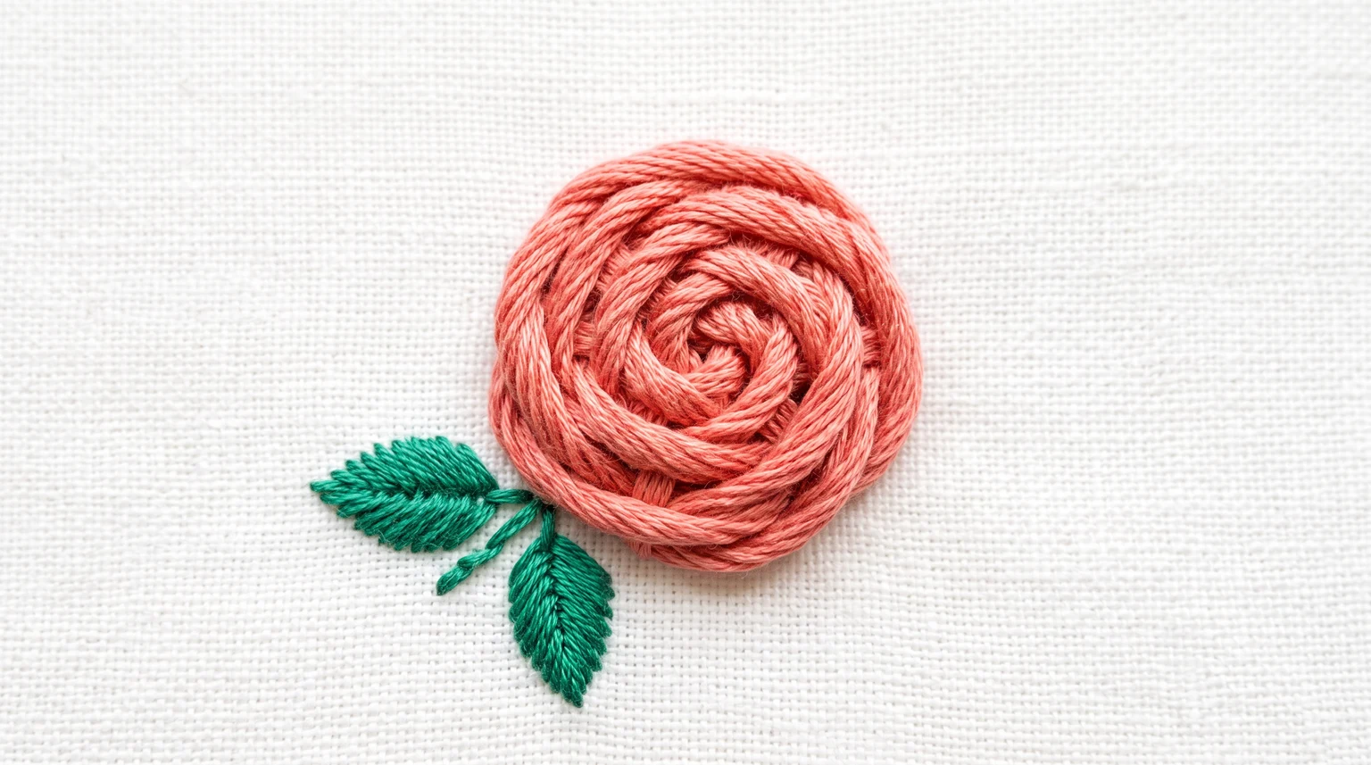 Raised coral woven rose with two green leaves on light fabric