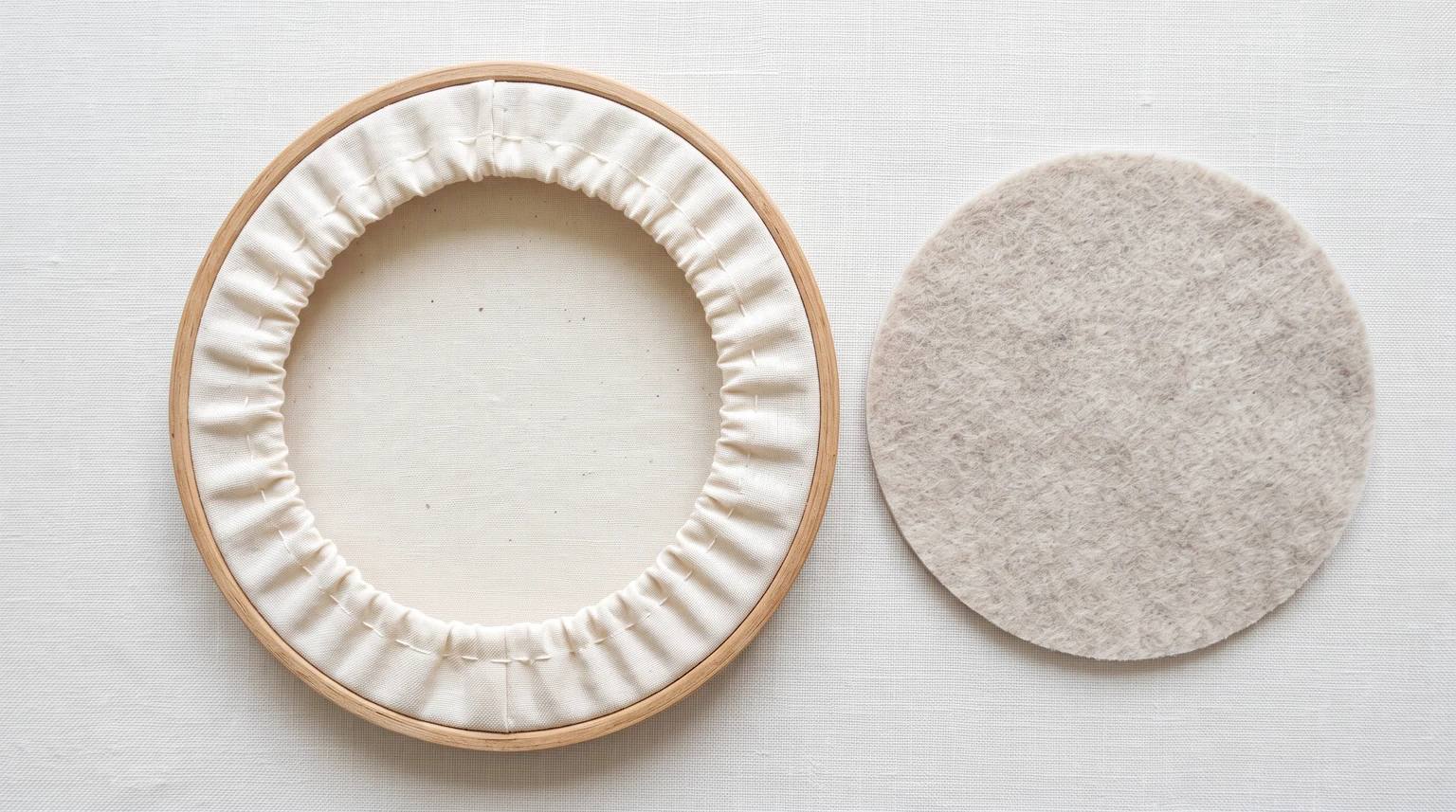 Back of a wooden hoop with fabric gathered inward beside a circular felt backing disk