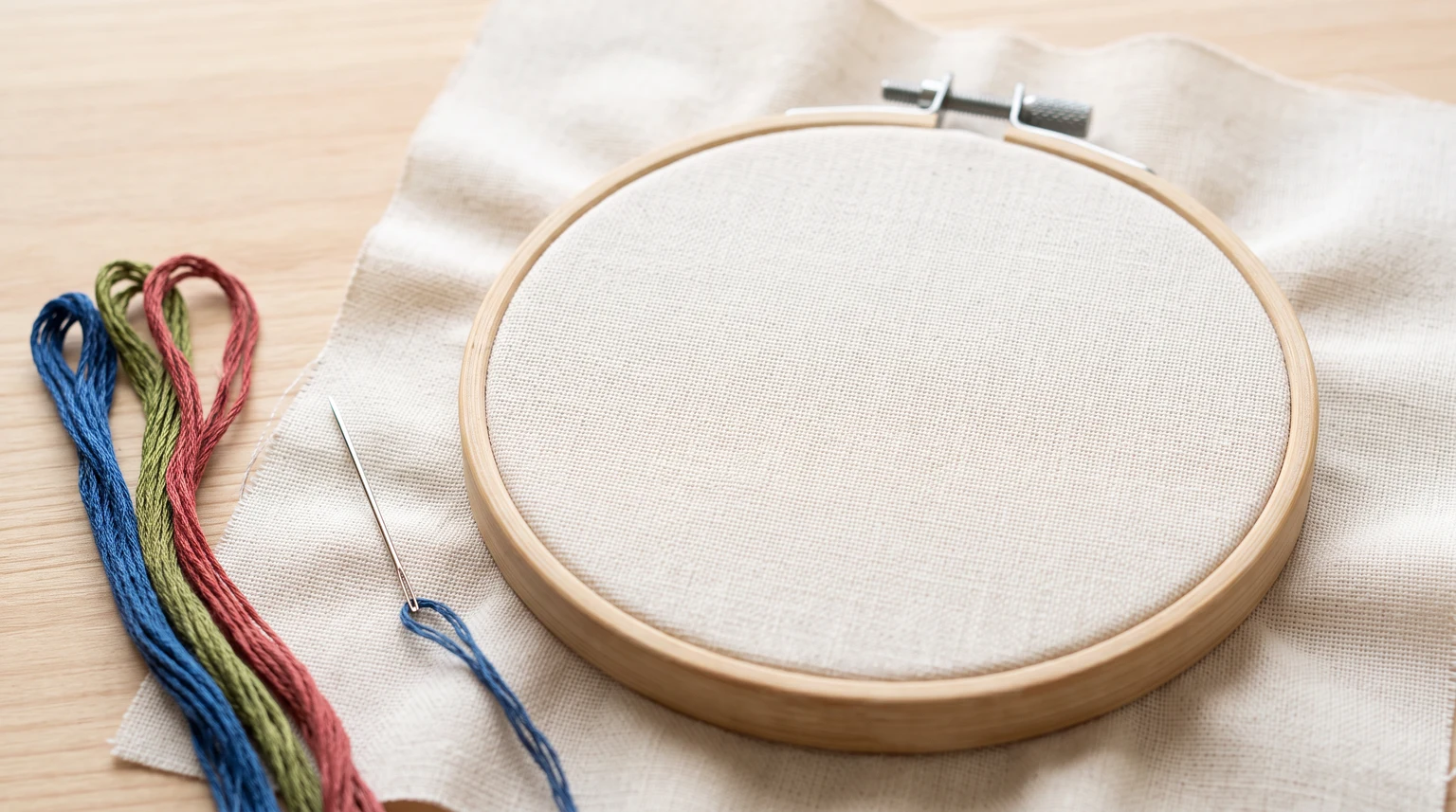Assembled wooden hoop holding smooth unmarked light fabric beside several floss colors
