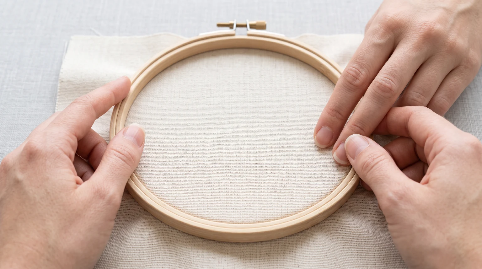 Hands smoothing the cloth near the rim of an assembled wooden hoop