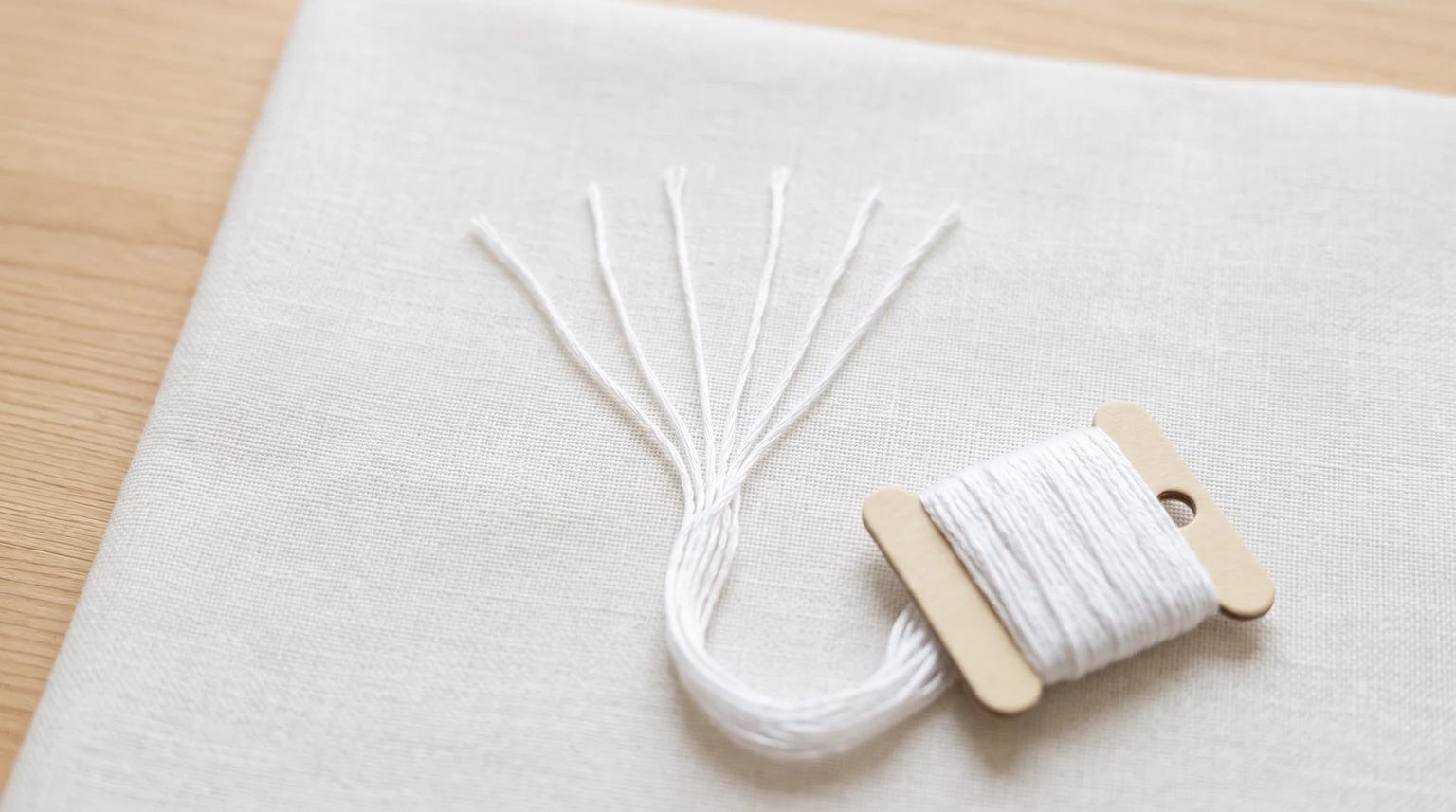 White cotton floss fanned into individual strands beside a thread bobbin