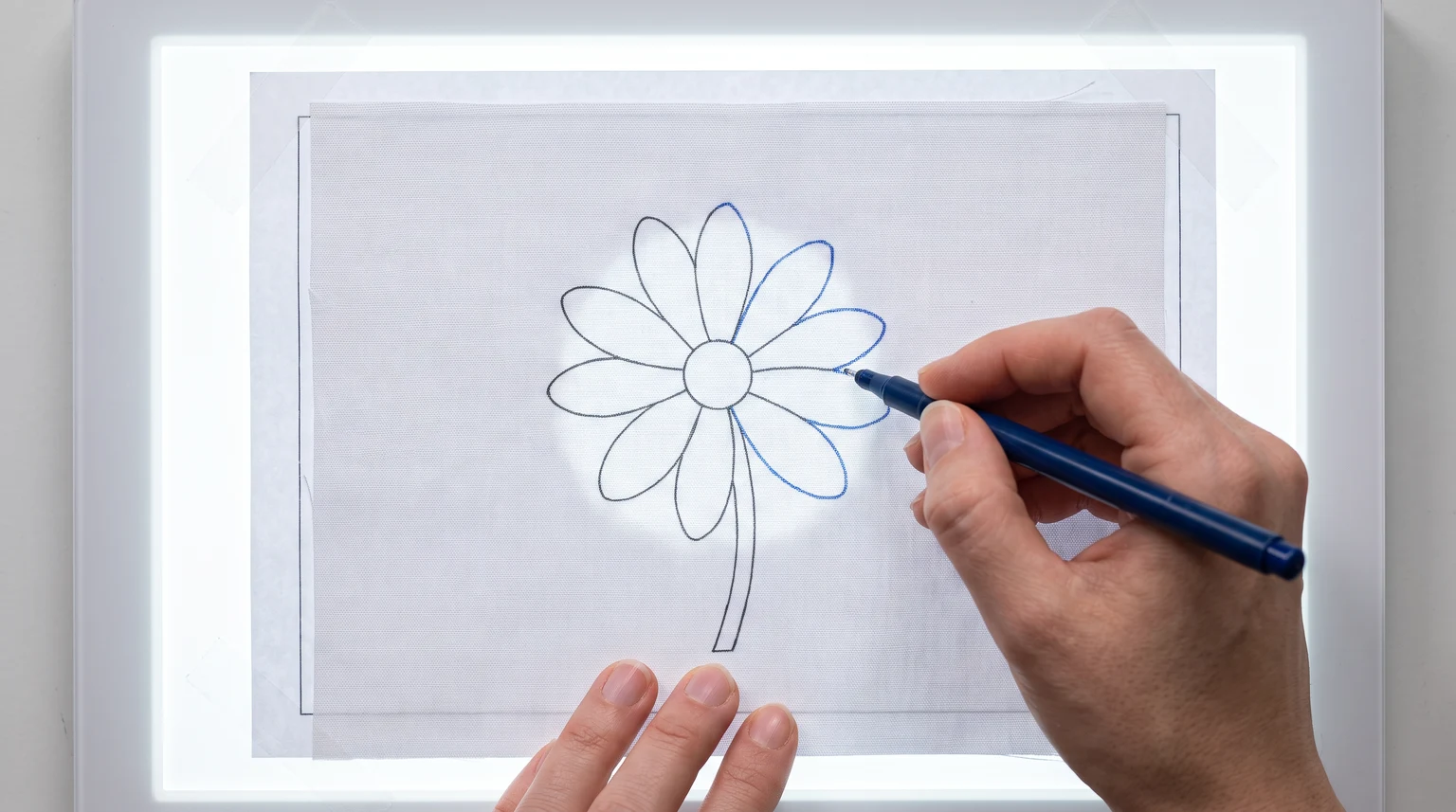 Hand tracing a flower outline through light fabric on an illuminated light pad