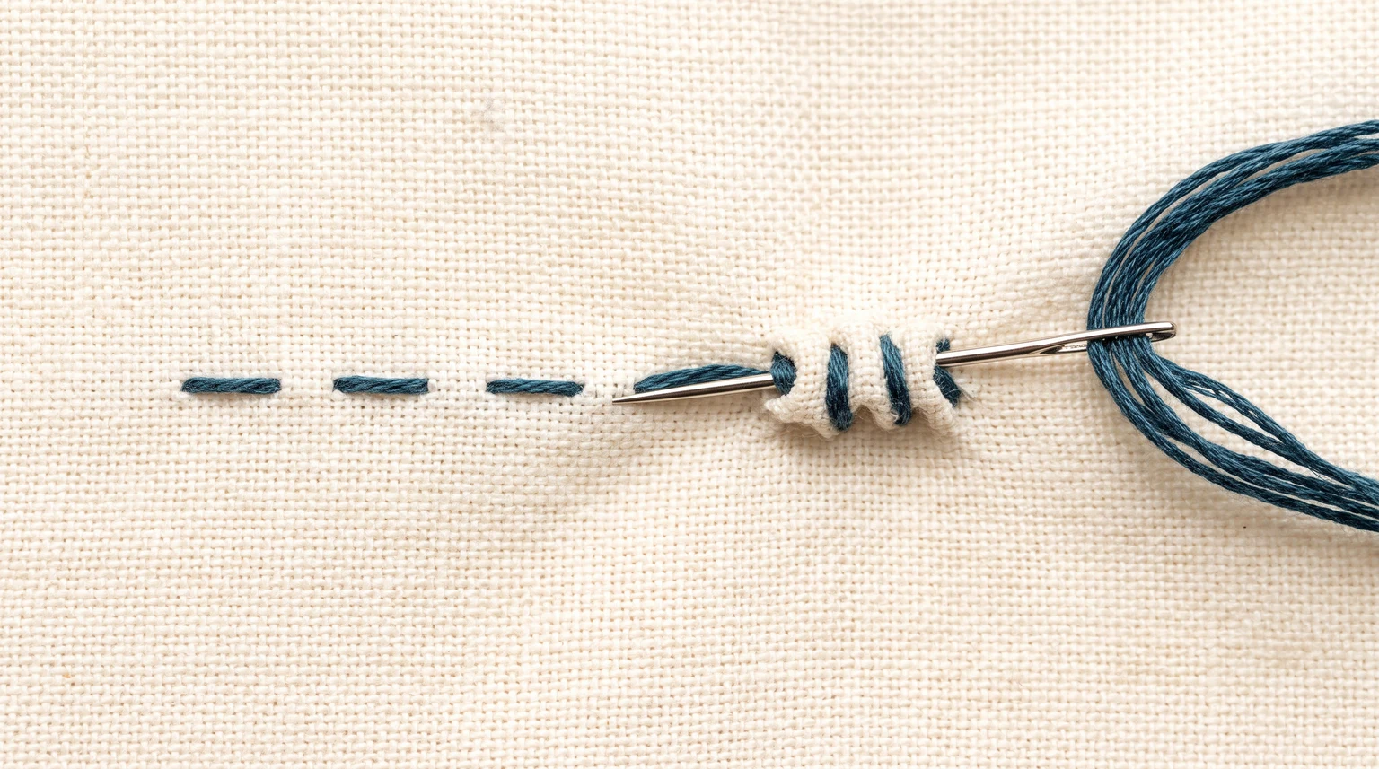Needle taking several small in-and-out passes through fabric beside completed blue running-stitch dashes