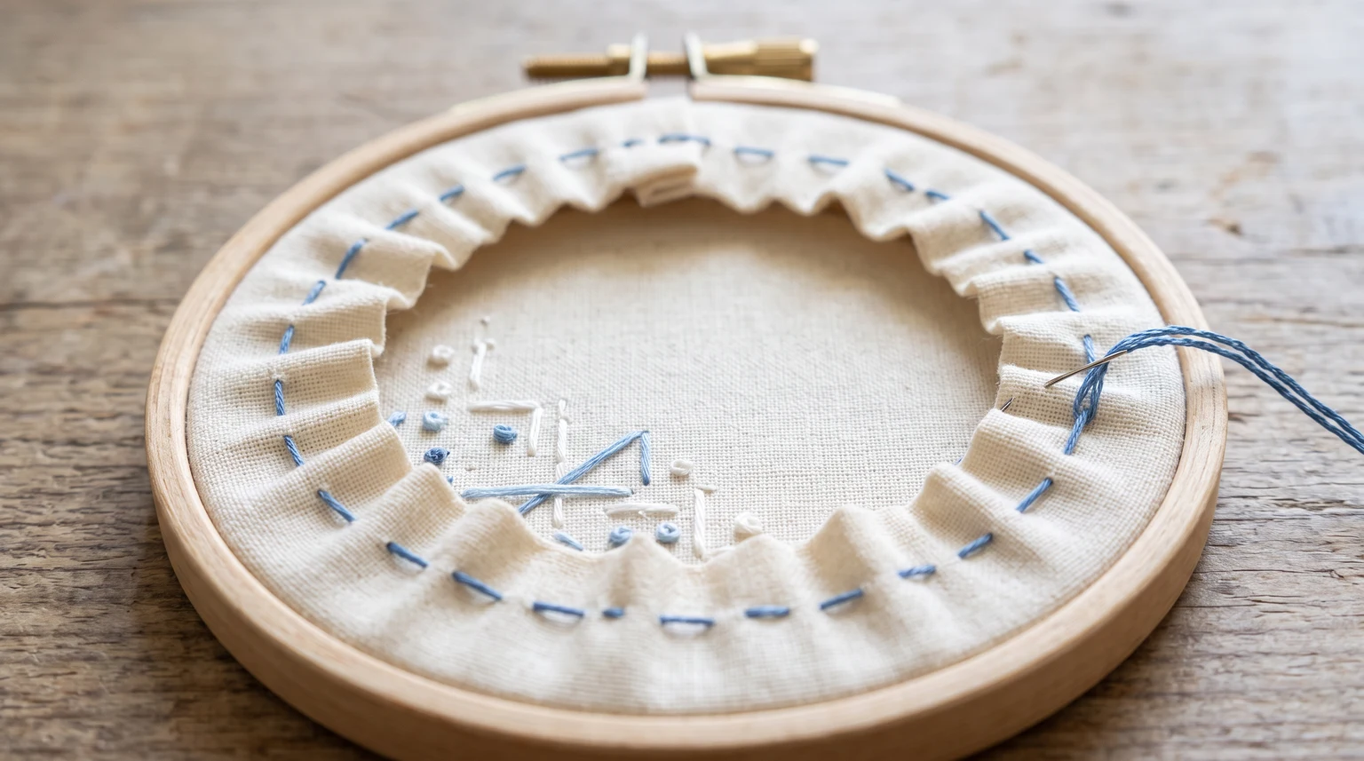 Back of a hoop with blue running stitches around the fabric allowance and part of the edge drawn into gathers
