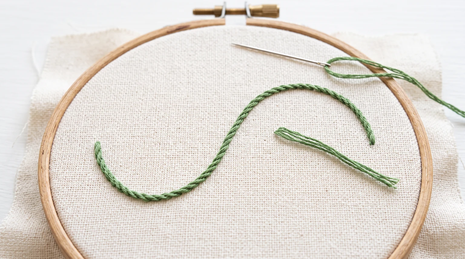 Fine rope-like green stitched line forming an S curve in a hoop