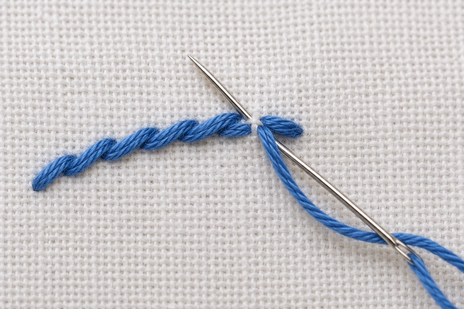 Macro view of overlapping blue outline stitches with a needle and working thread below the line
