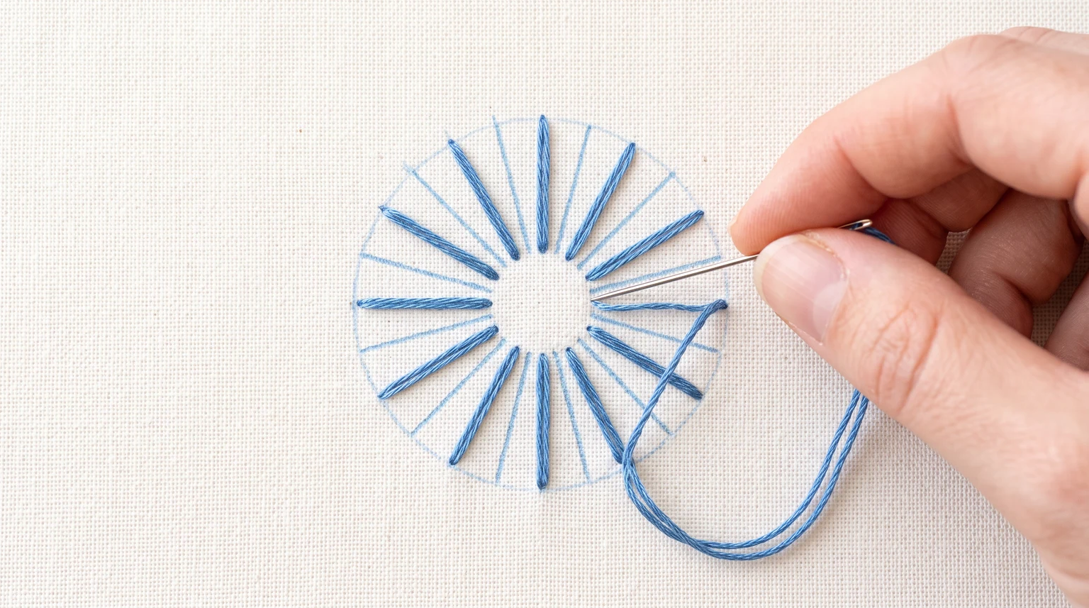 Blue straight-stitch rays around an empty circular center with a working needle nearby